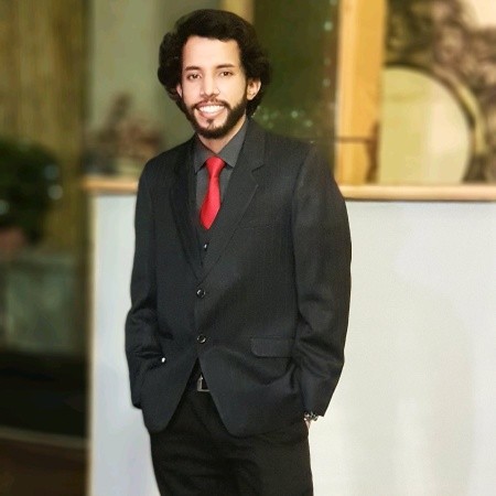 Adrian Banerjee in a black suit with a red tie.